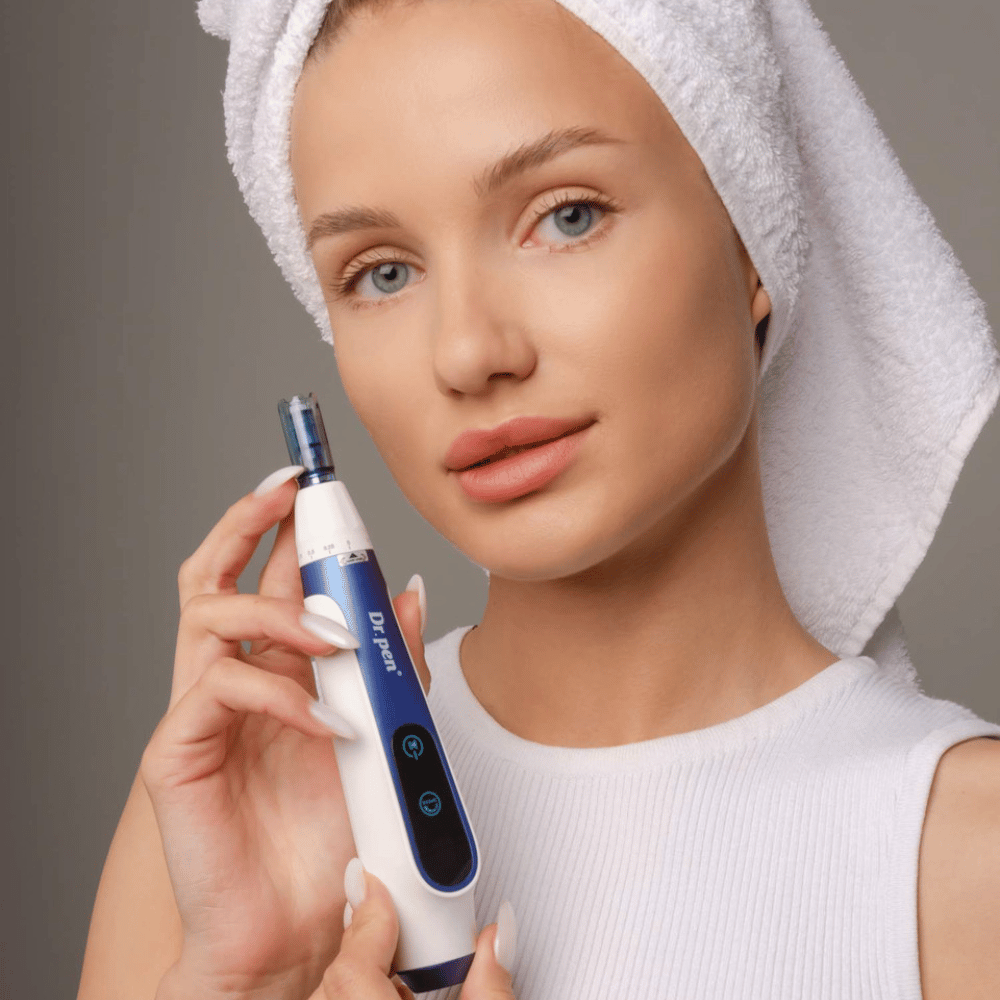 Mujer con toalla alrededor del cabello sosteniendo una pluma Dr. Pen A11 microneedling - dispositivo profesional de cuidado de la piel para una piel más lisa y firme.